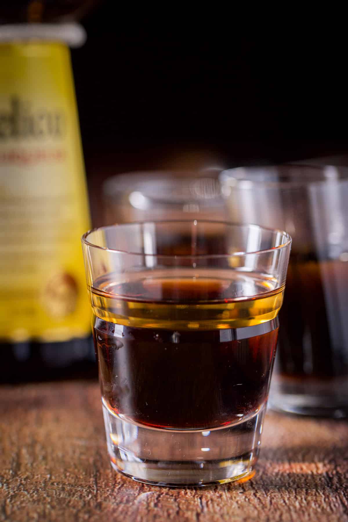 Frangelico layered into the glass in a layer with the bottle and the other glasses behind it