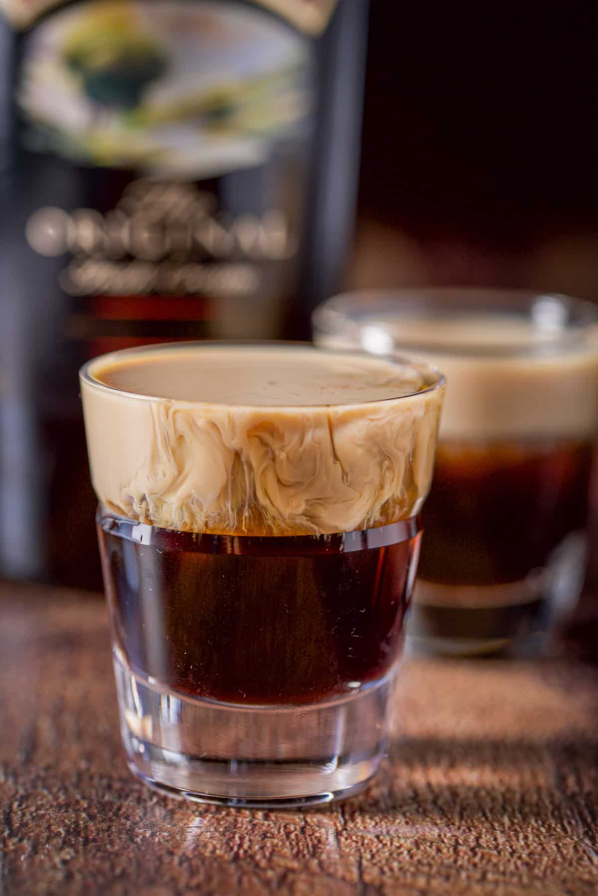 Baileys layered into the beveled glass with another glass and the bottle in the background