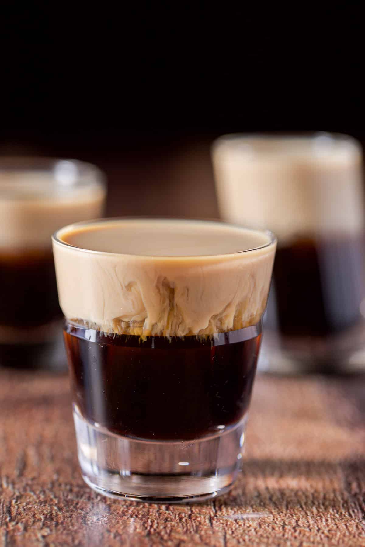 Close up of the beveled glass filled with the layered shot in front of the two other shot glasses