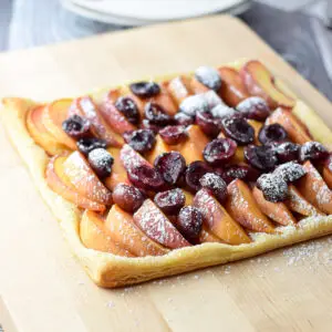 A board with cherries and peaches on a puff pastry - square