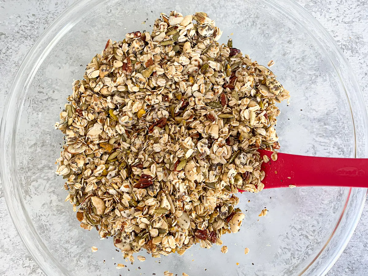 Overhead view of the granola ingredients stirred together with a red spatula in the bowl