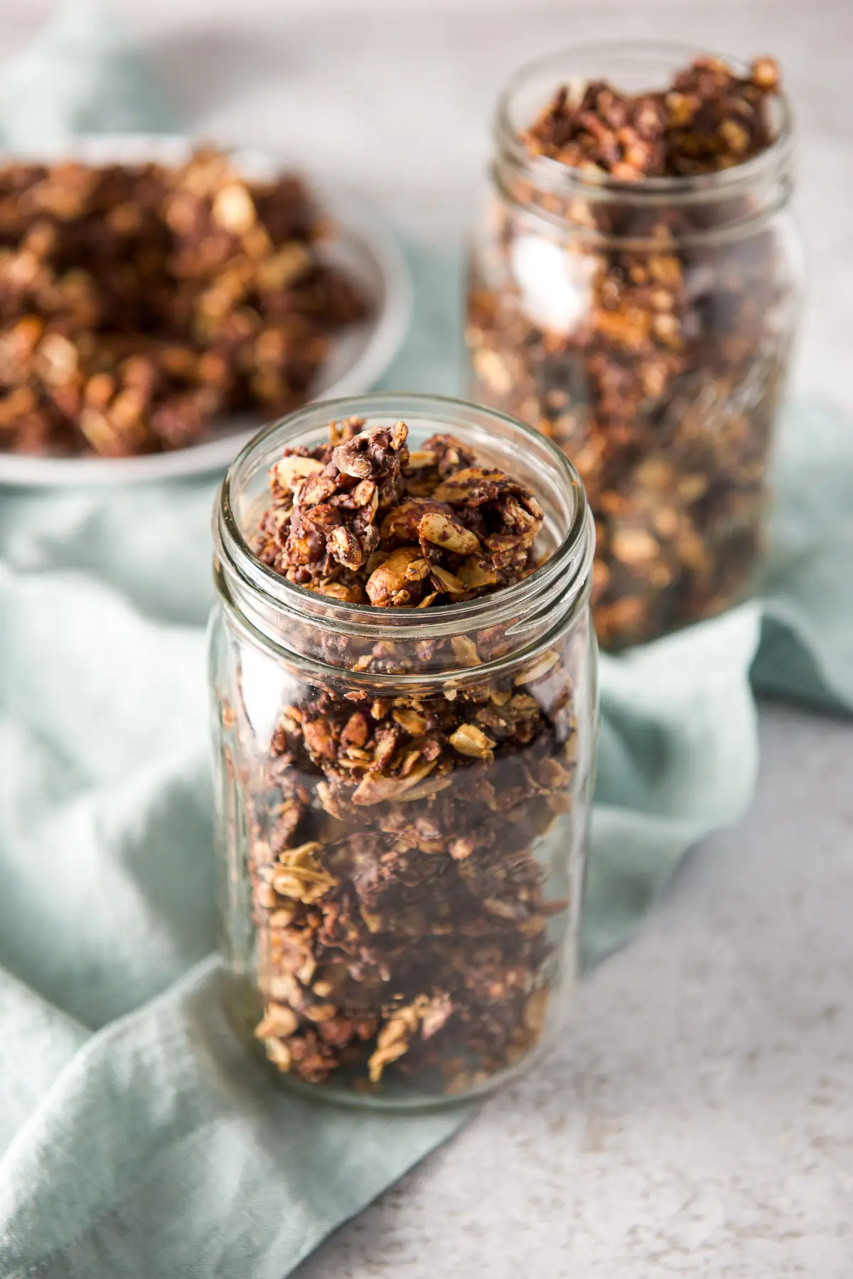 Two jars of clusters in it and a white plate with more granola in the background