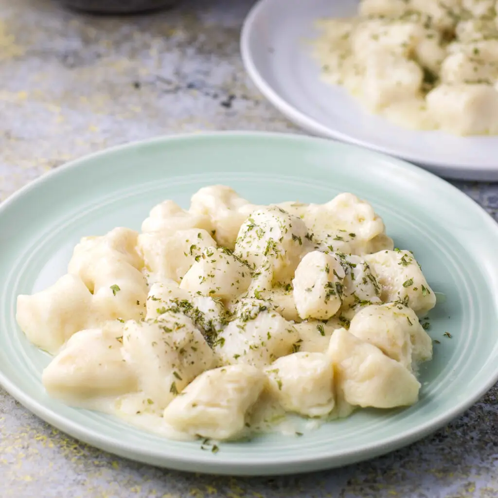 A green plate with gnocchi with sauce and parsley on it - square