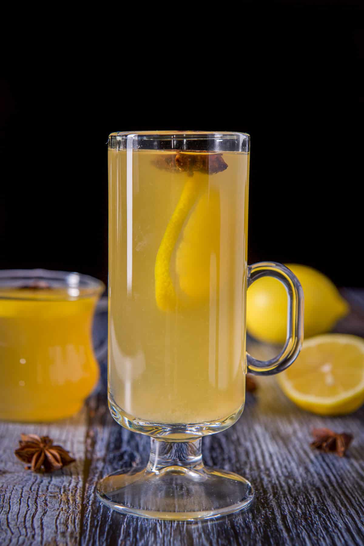 Tall glass mug in front of the shorter one, both filled with the lemon cocktail, star anise and lemon wheels for garnish