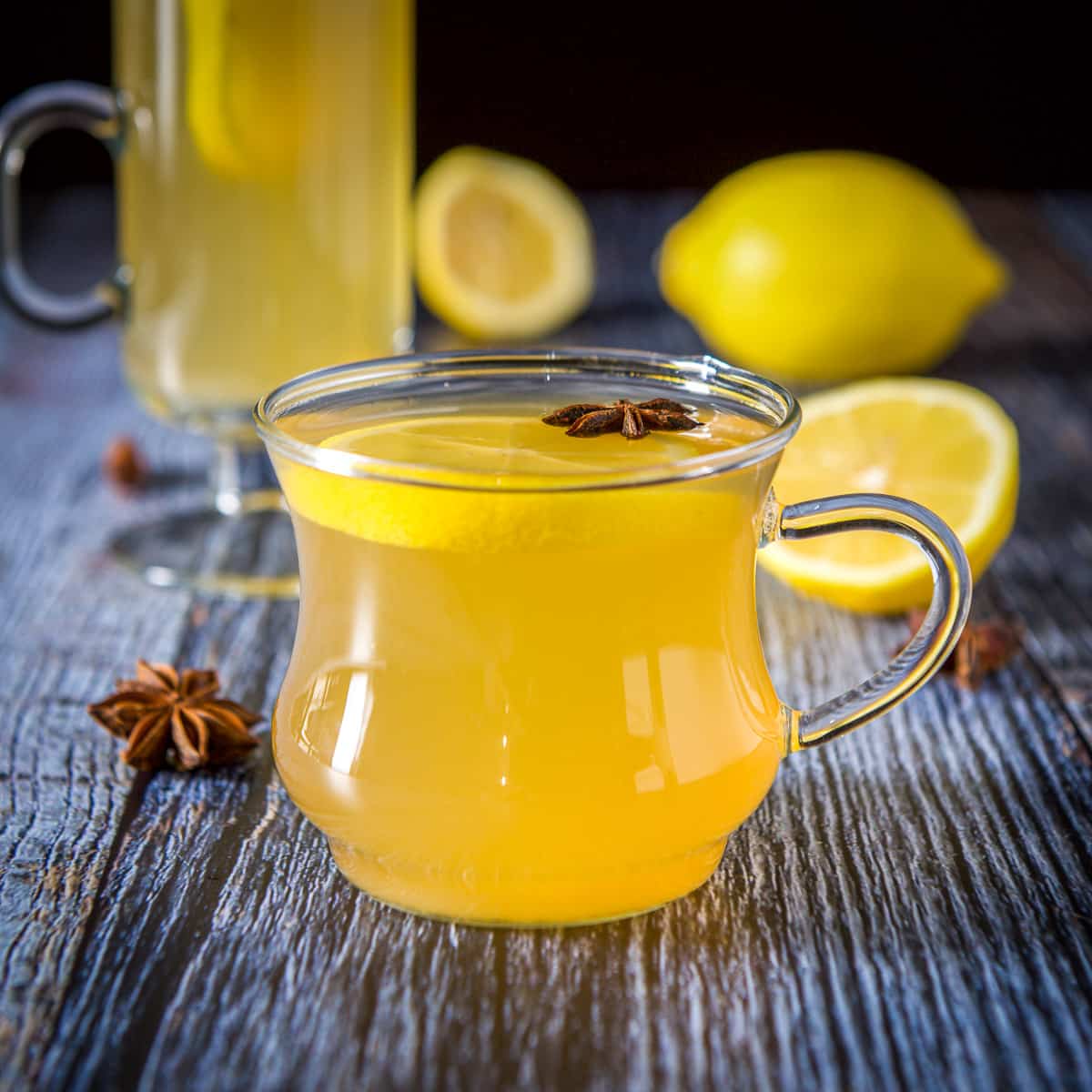 The short glass mug filled with a golden drink with star anise and a lemon wheel in it - square
