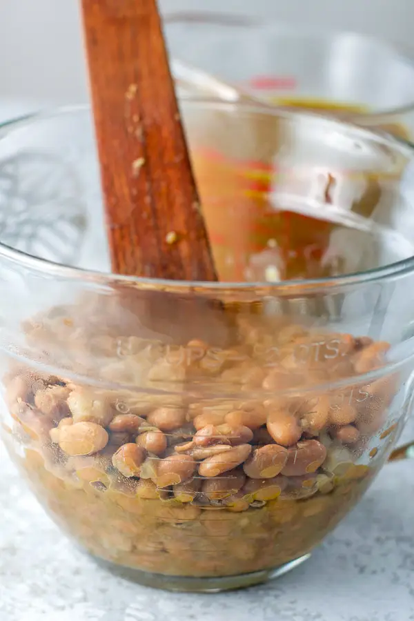 Pinto beans in a glass bowl with a wooden utensil