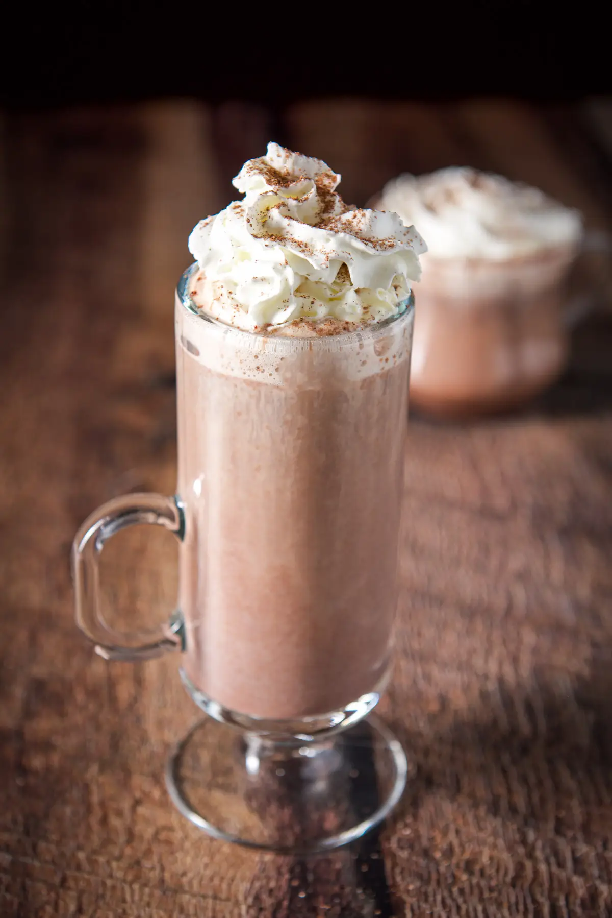 Two mugs with hot chocolate in them with whipped cream and sprinkled chocolate on top