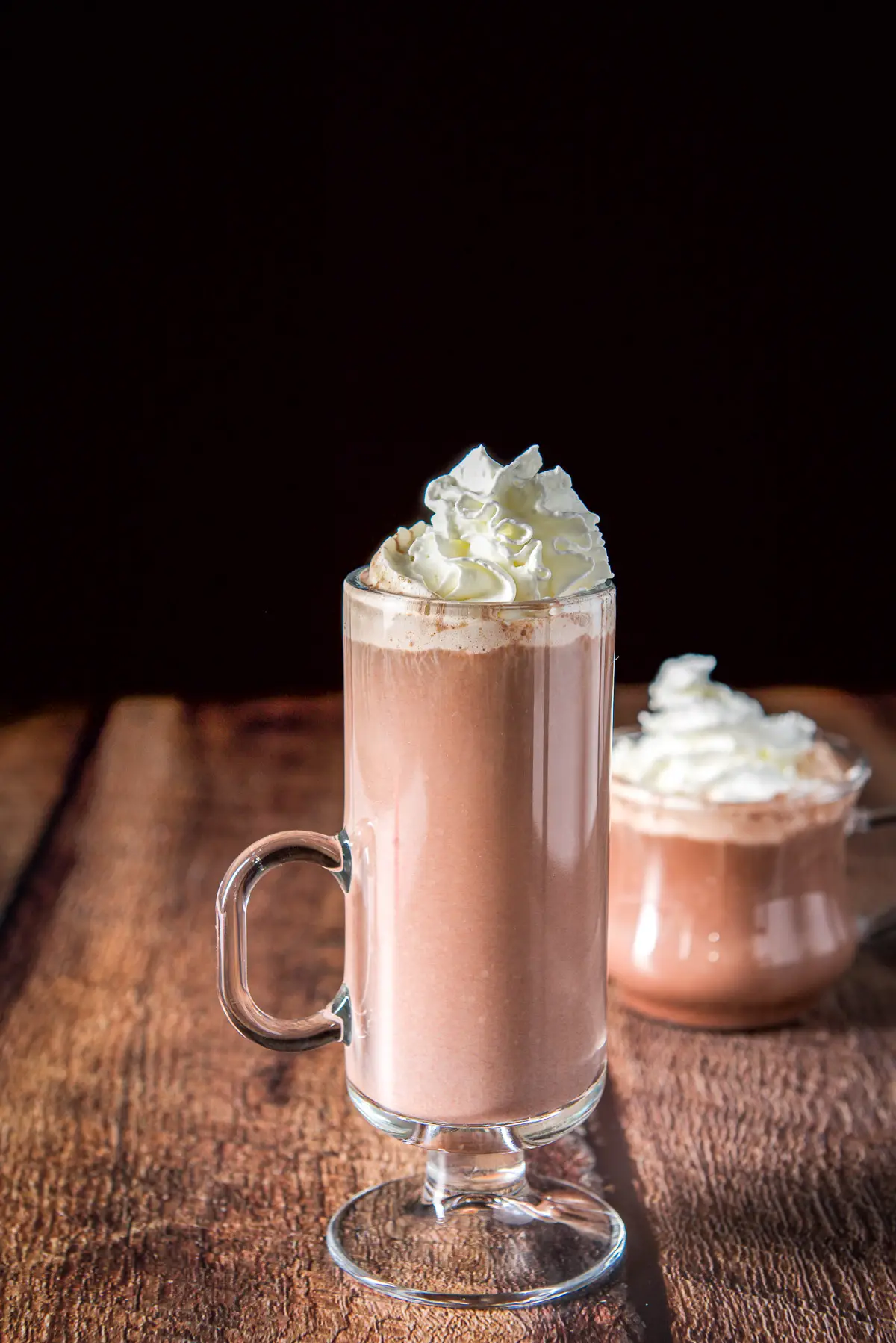 Two glass mugs filled with the chocolate drink with whipped cream on top