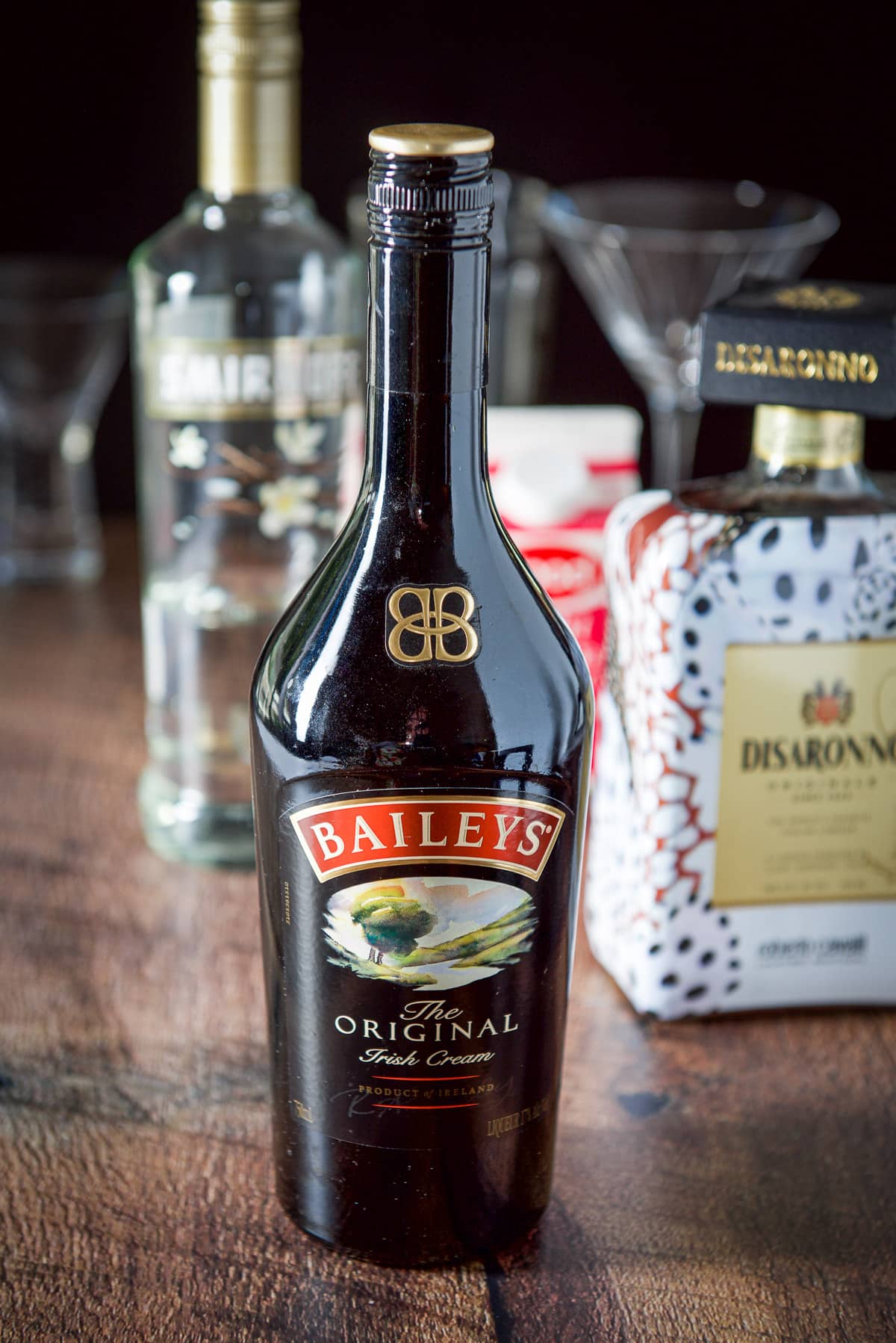 Baileys, vanilla vodka, Amaretto and cream in the background with the shaker and glasses