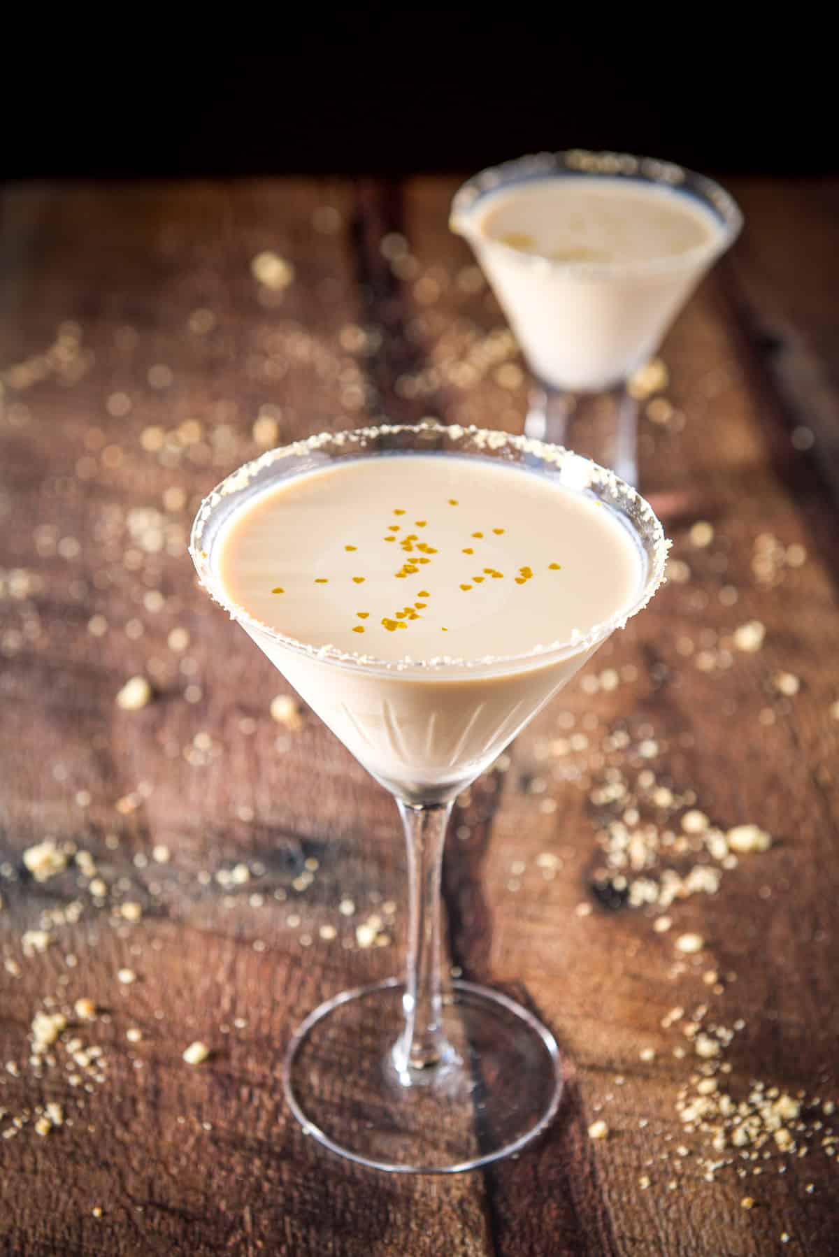 A classic martini glass with the cookie martini with a cookie crumb garnish with floating gold hearts