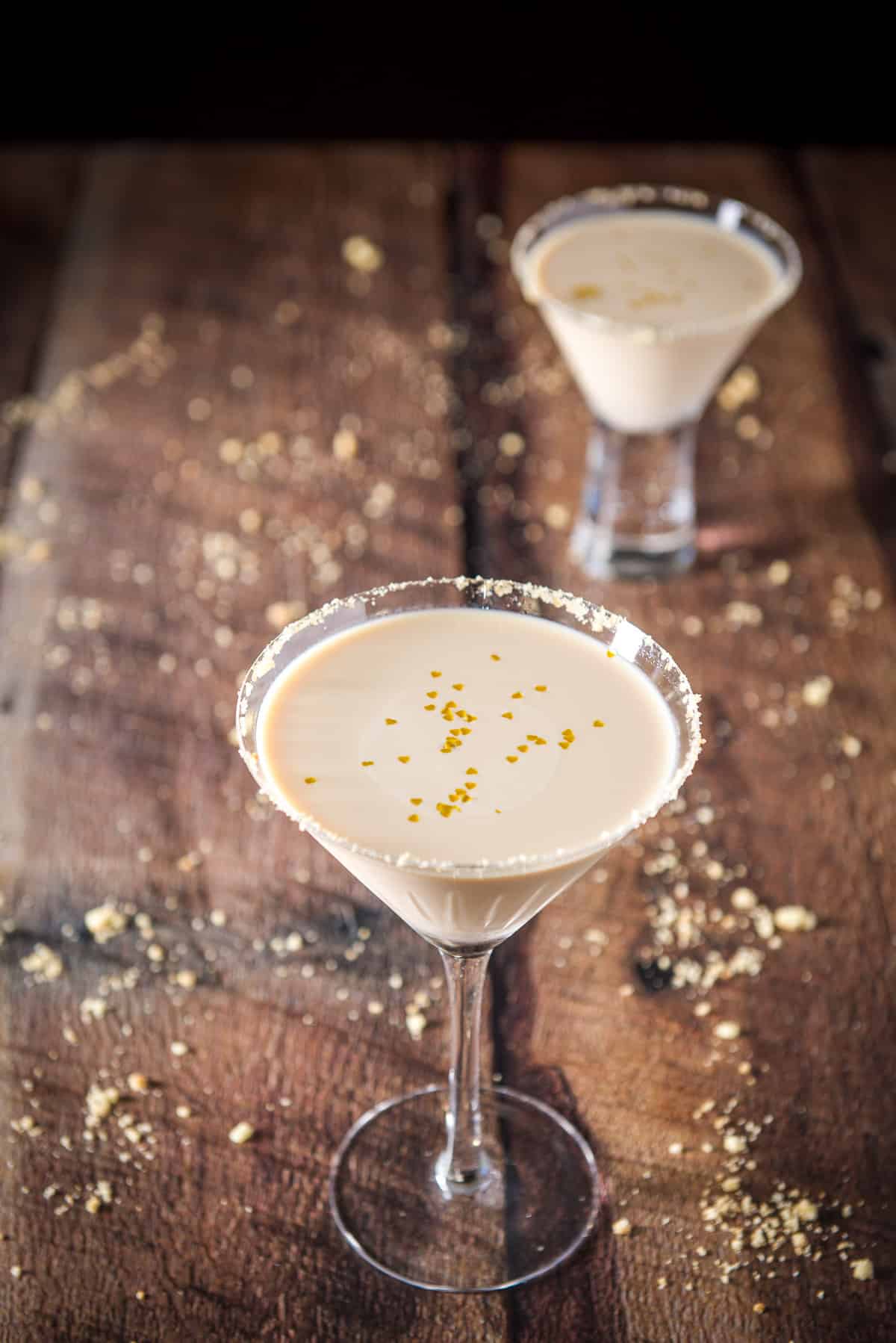 High view of the classic martini glass with the cookie martini with gold hearts floating on the surface. There is another glass in the background