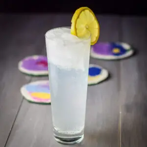 A tall flared glass filled with the collins. THere is a lemon wheel on the rim - Square