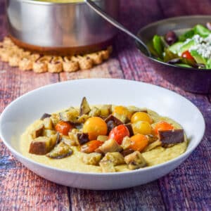 a white plate with polenta and tomatoes and eggplant - square