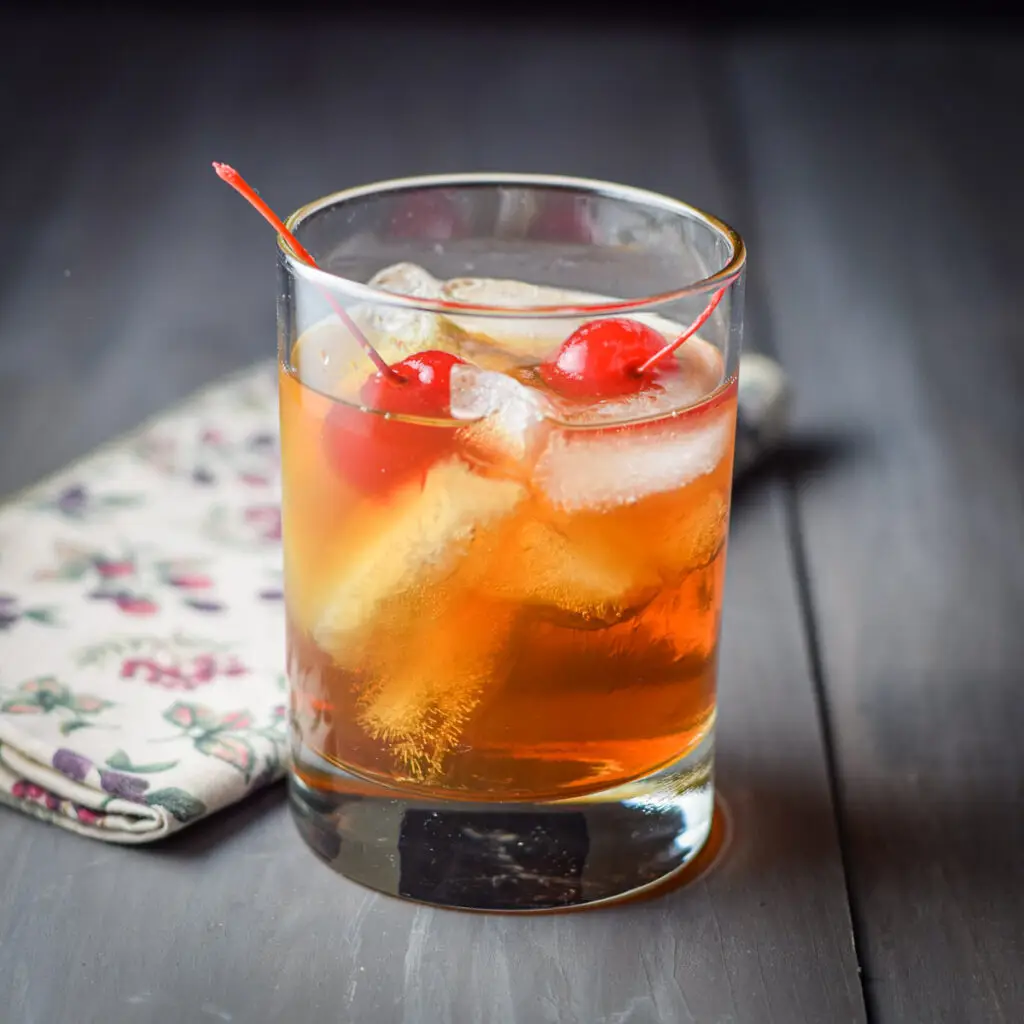 A double old fashioned glass filled with the Manhattan with two cherries in it - square