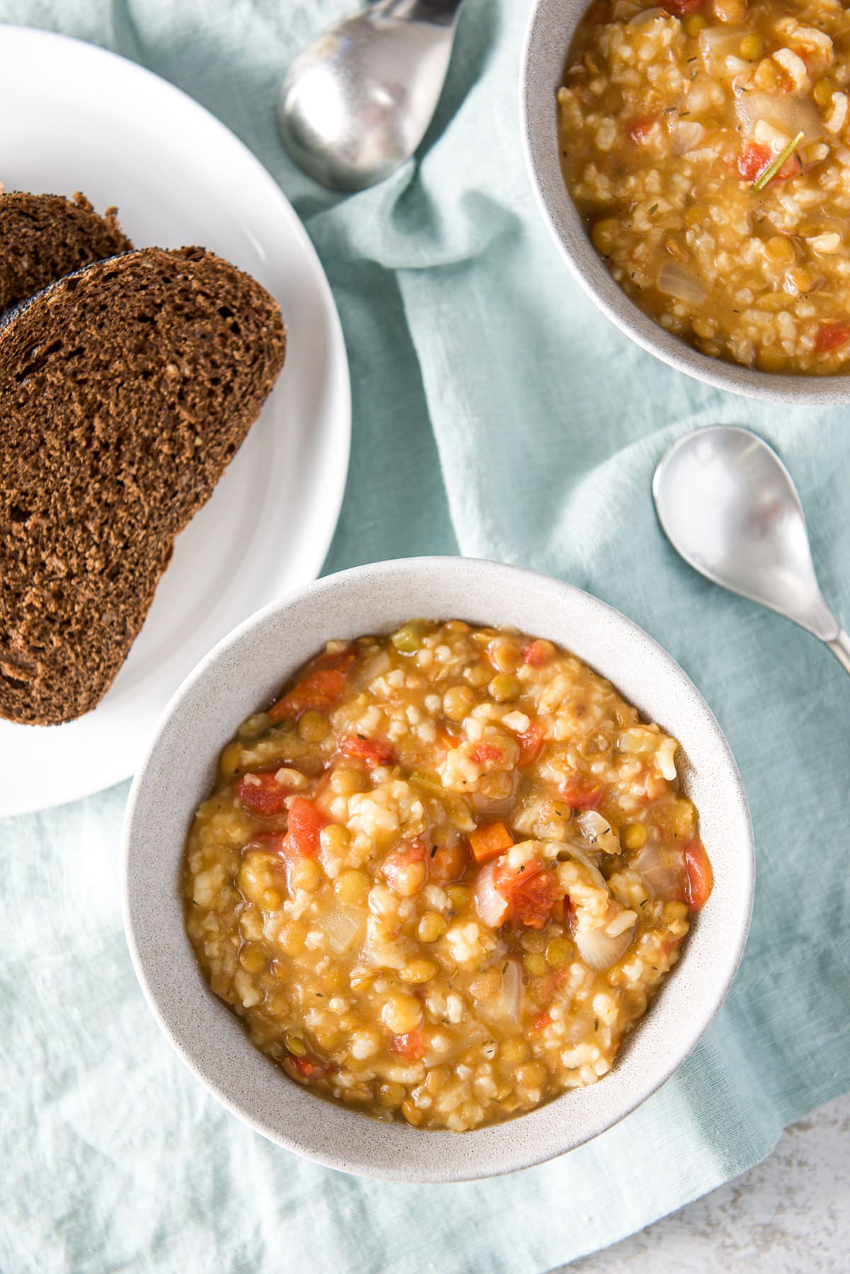 Overhead view of the bowls with the thick chunky soup with a white plate of dark bread