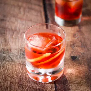 A bubble glass filled with the red cocktail with a twist in it - square