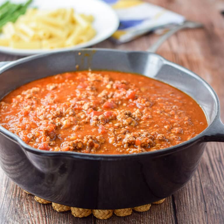 Gravy in a cast iron pan with a white plate with pasta in the background - square