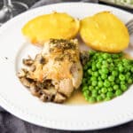 A white beaded plate with a chicken thigh with mushrooms and sauce, peas and baked potato - square