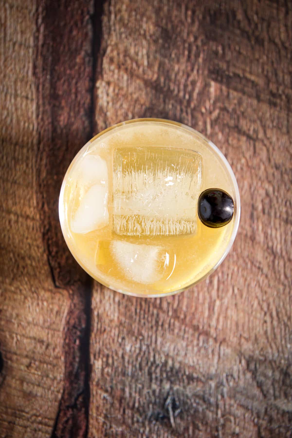 Overhead view of a glass with a lemon cocktail with a big ice cube and cherry on top