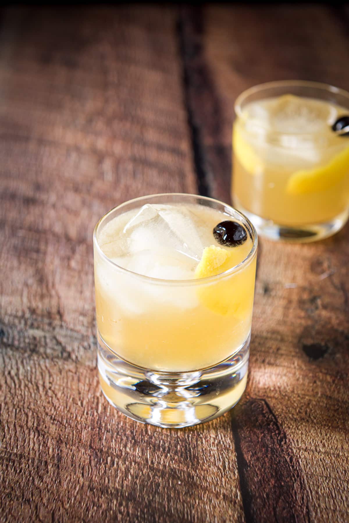 A bubble glass in front filled with the lemon cocktail with the other glass in the back