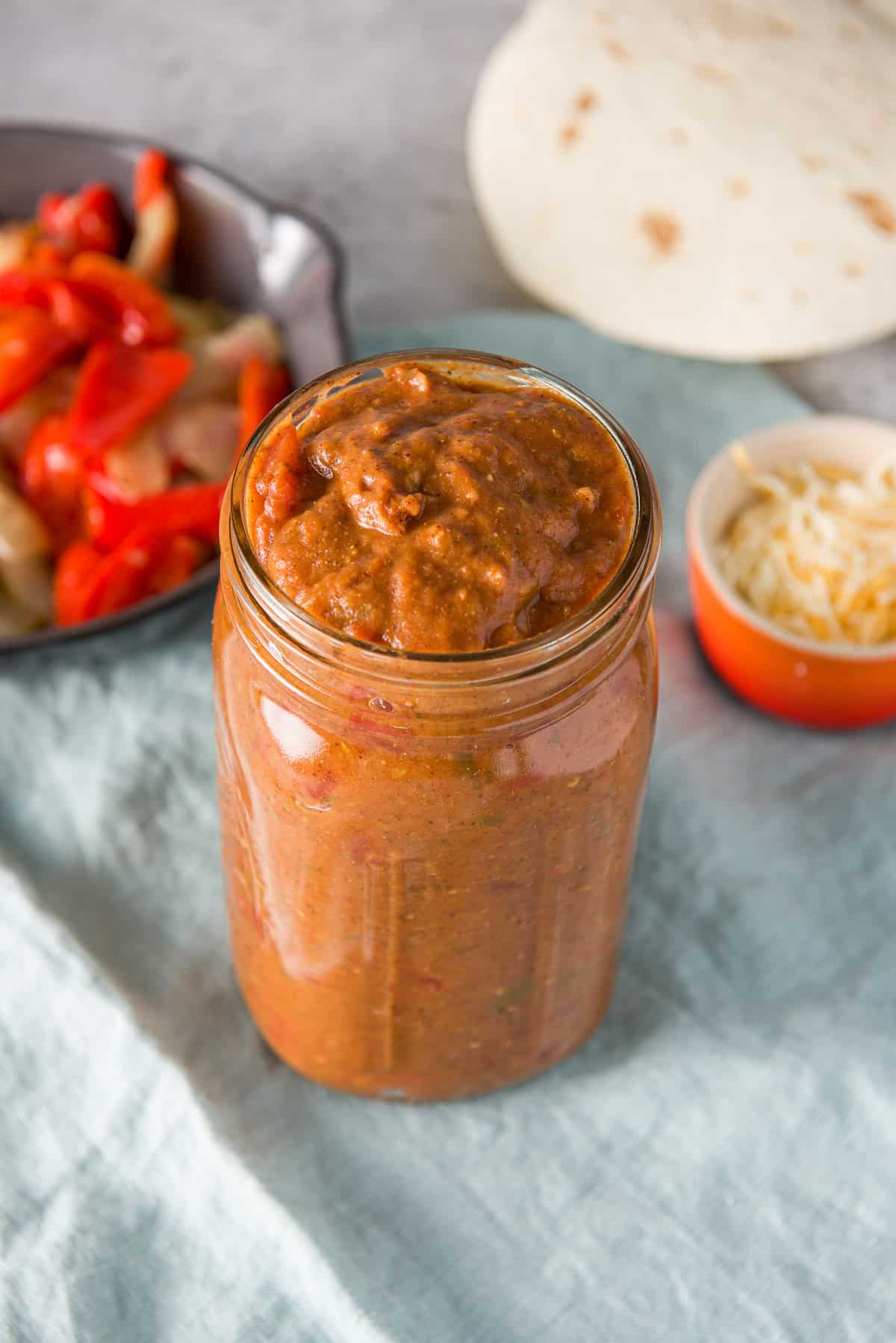 Near overhead view of the sauce in the jar, cheese, tortillas and vegetables