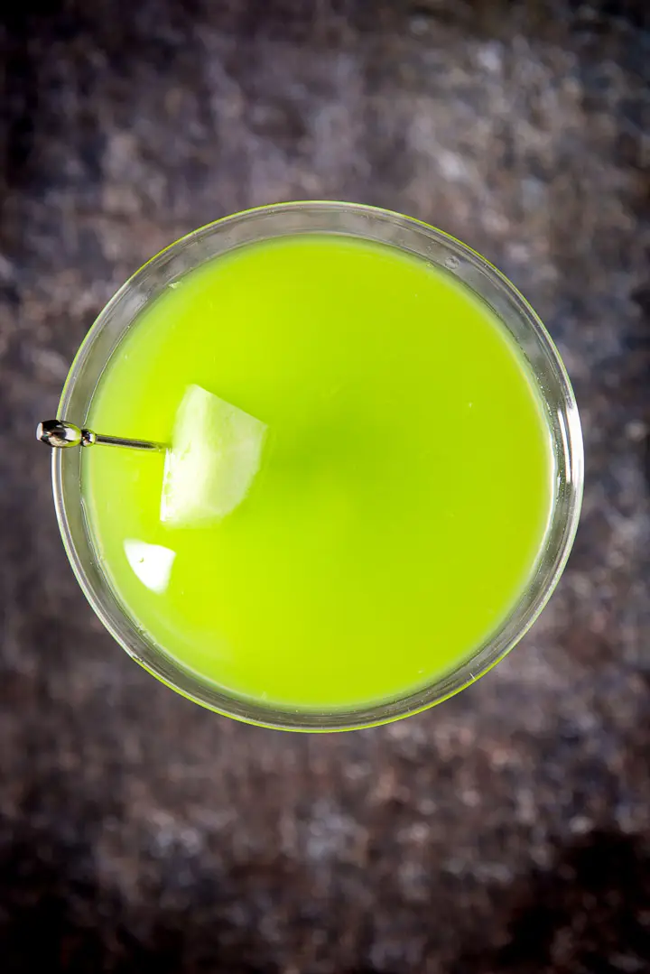 Overhead view of the green cocktail in the martini glass with melon on a pick