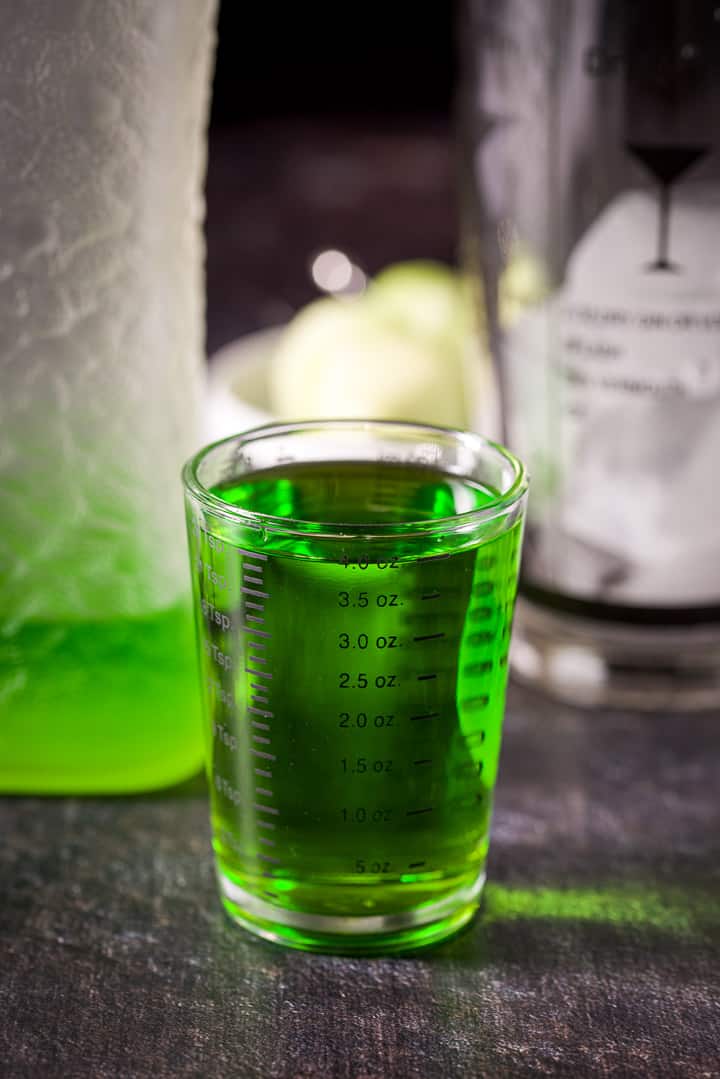 Melon liqueur measured out with the bottle and ice filled shaker in the background