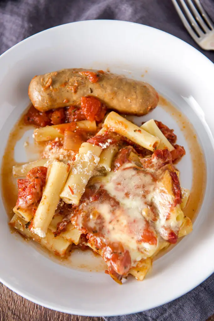 Overhead view of a white deep plate with ziti, cheese and a sausage