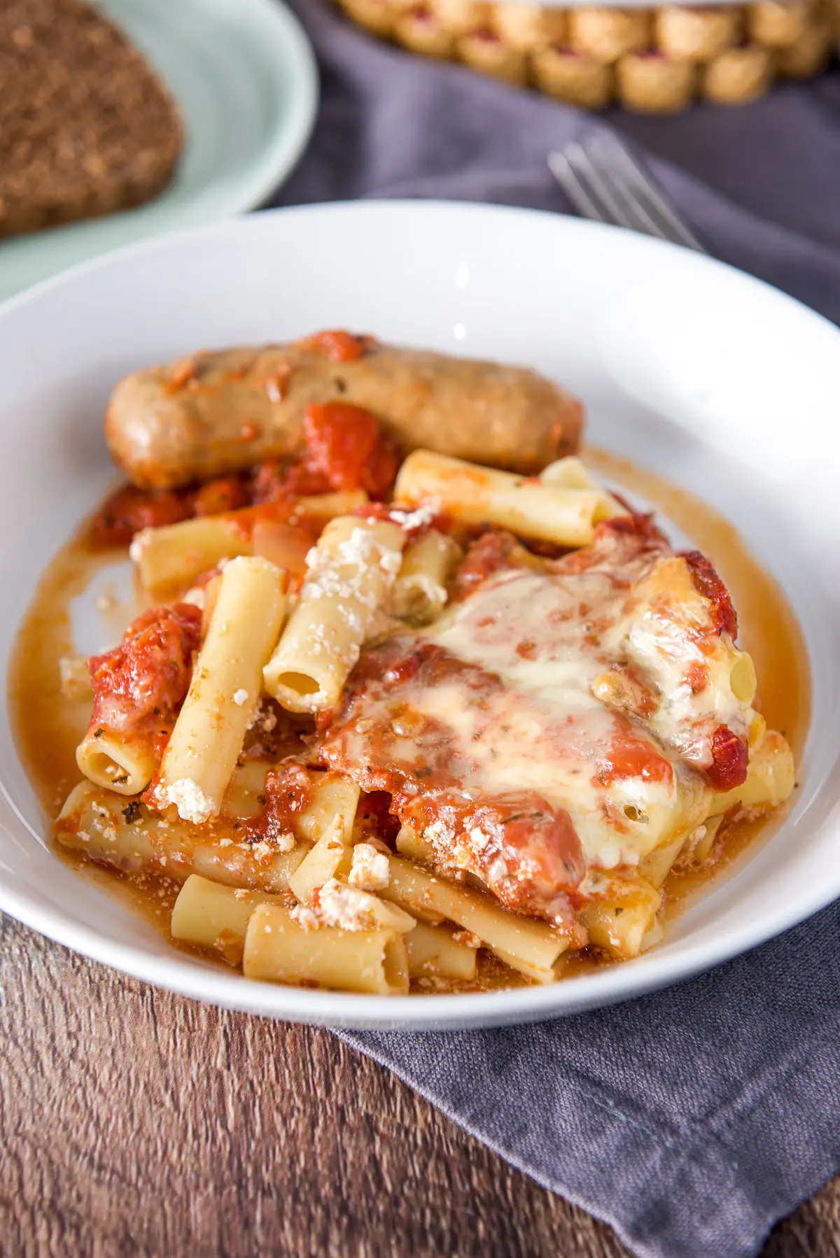 Close up view of a plate of ziti with cheese and a sausage