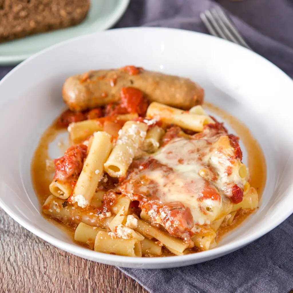 A white deep plate with tomato, cheese ziti and a sausage - square