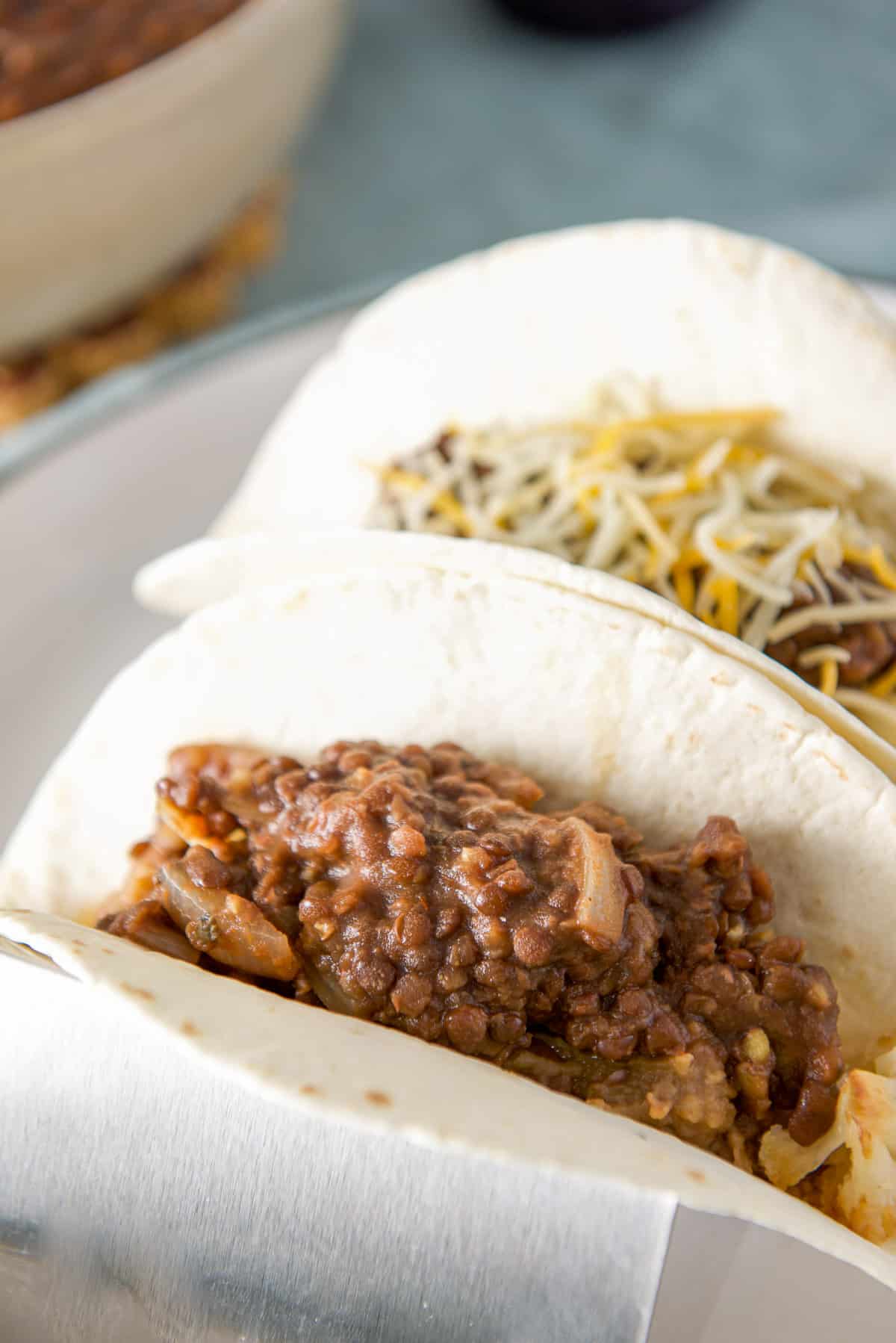 Close up of two flour tortillas in a taco holder with the lentils - one with cheese the other without