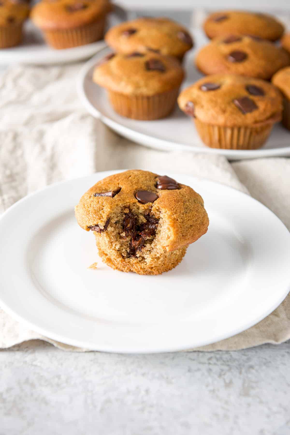 A white plate with a muffin with a bite taken out of it. There are more plates of muffins in the background