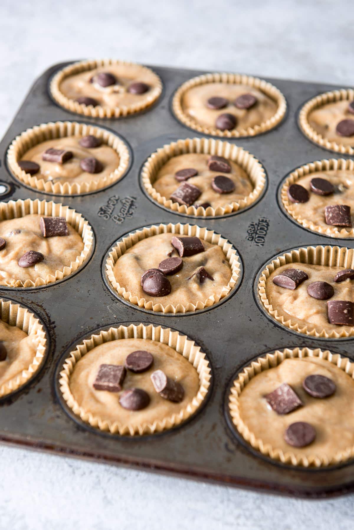Muffin batter with chocolate chips on top in baking cups in the tin