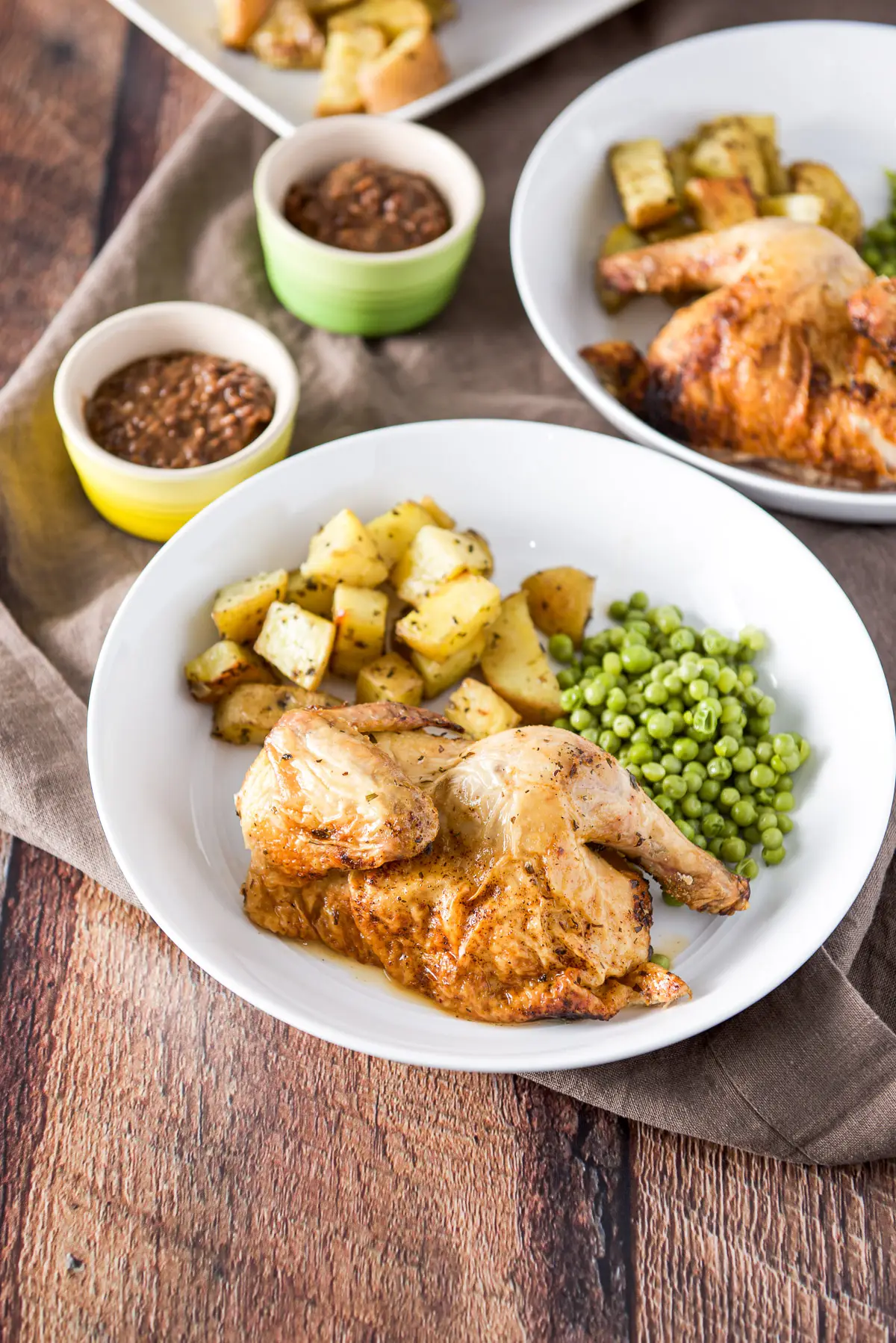 A deep white plate with half of a hen on it with potatoes and peas