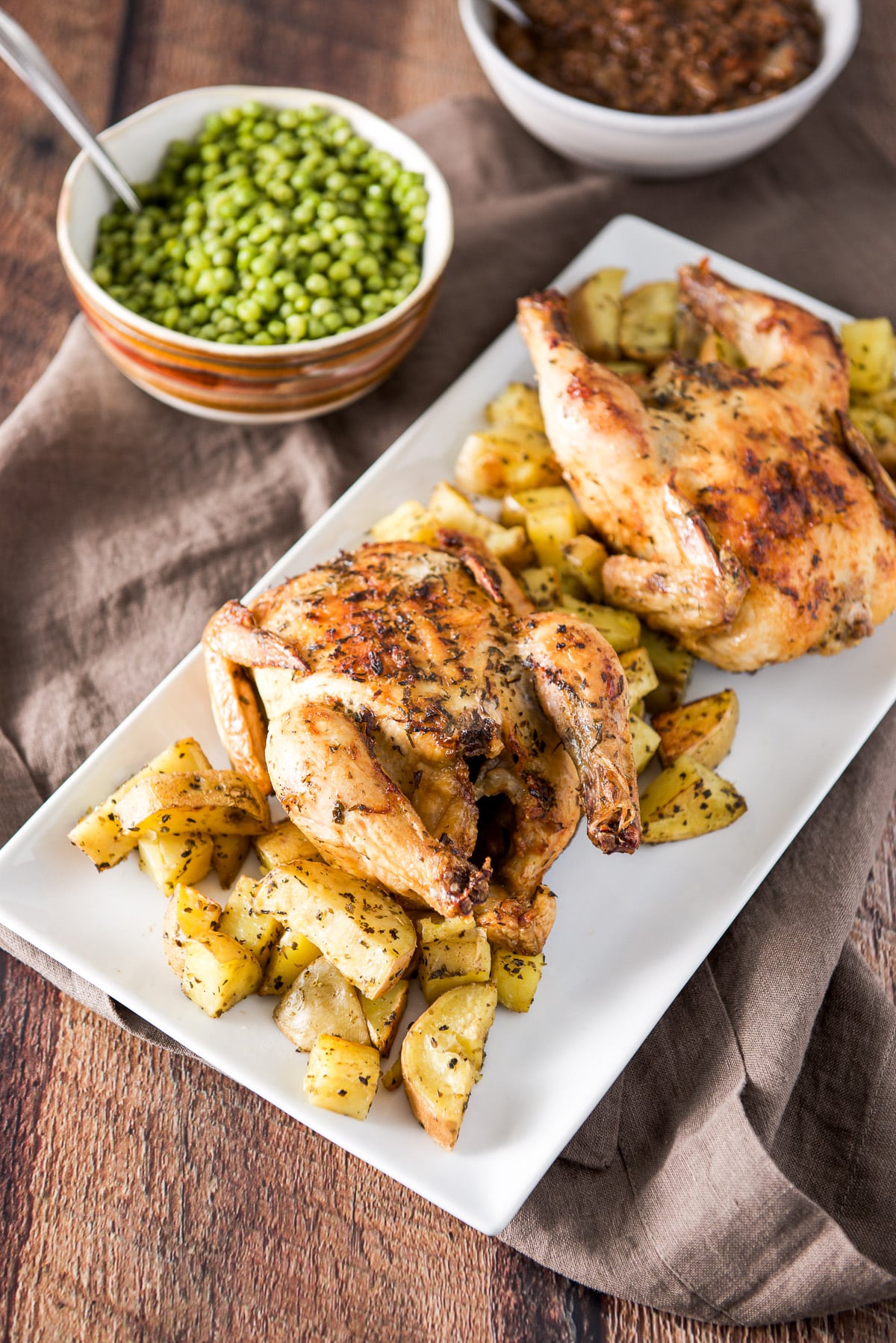 Two hens, one with the legs facing front with the other facing back. There are herb potatoes on the platter as well