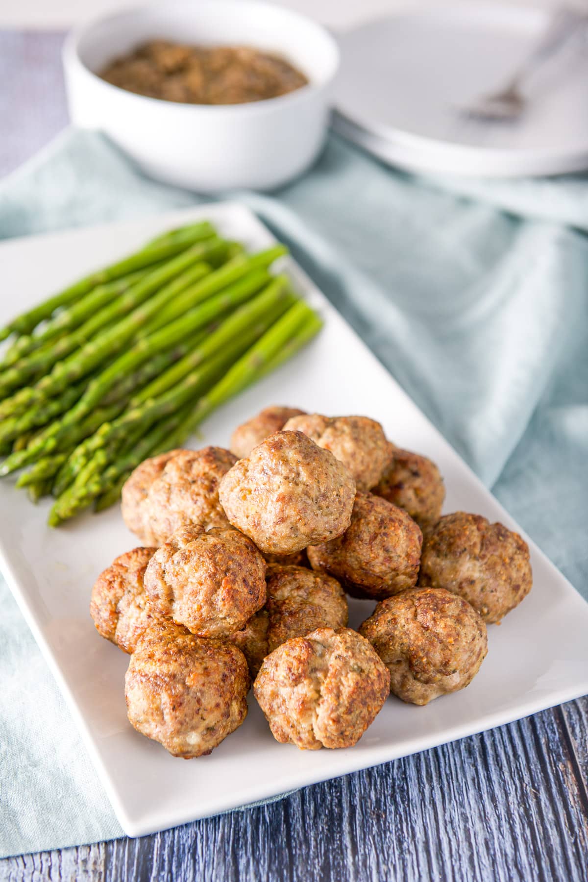 A white rectangle with a pile of meatballs and asparagus on it and lentils in the background