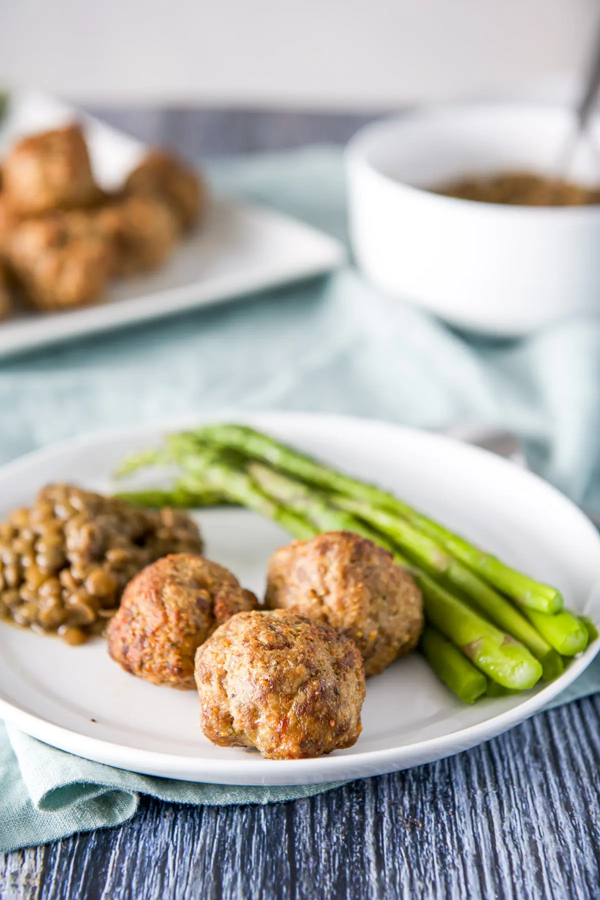 A white plate with three meatballs, asparagus and lentils