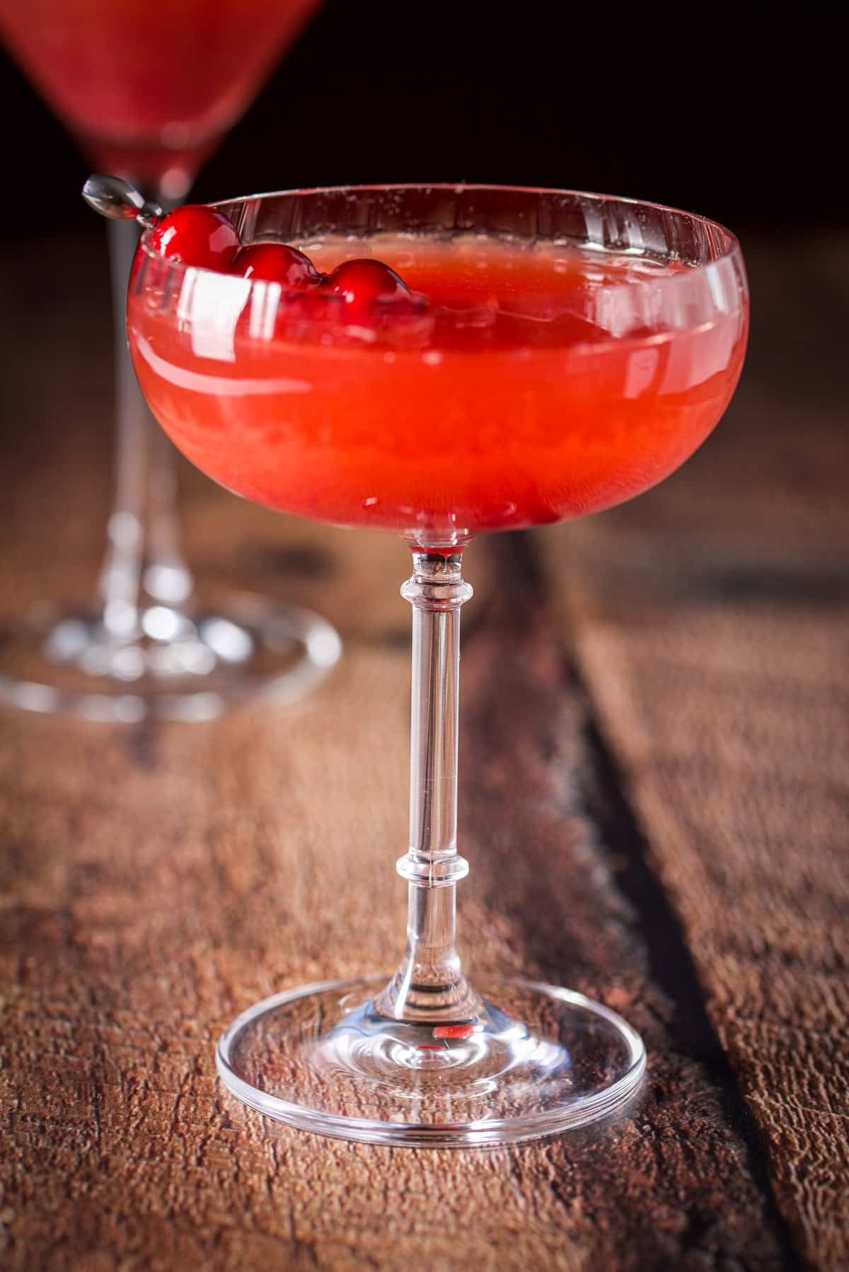 A coupe glass filled with the red cocktail with cranberries on a martini pick