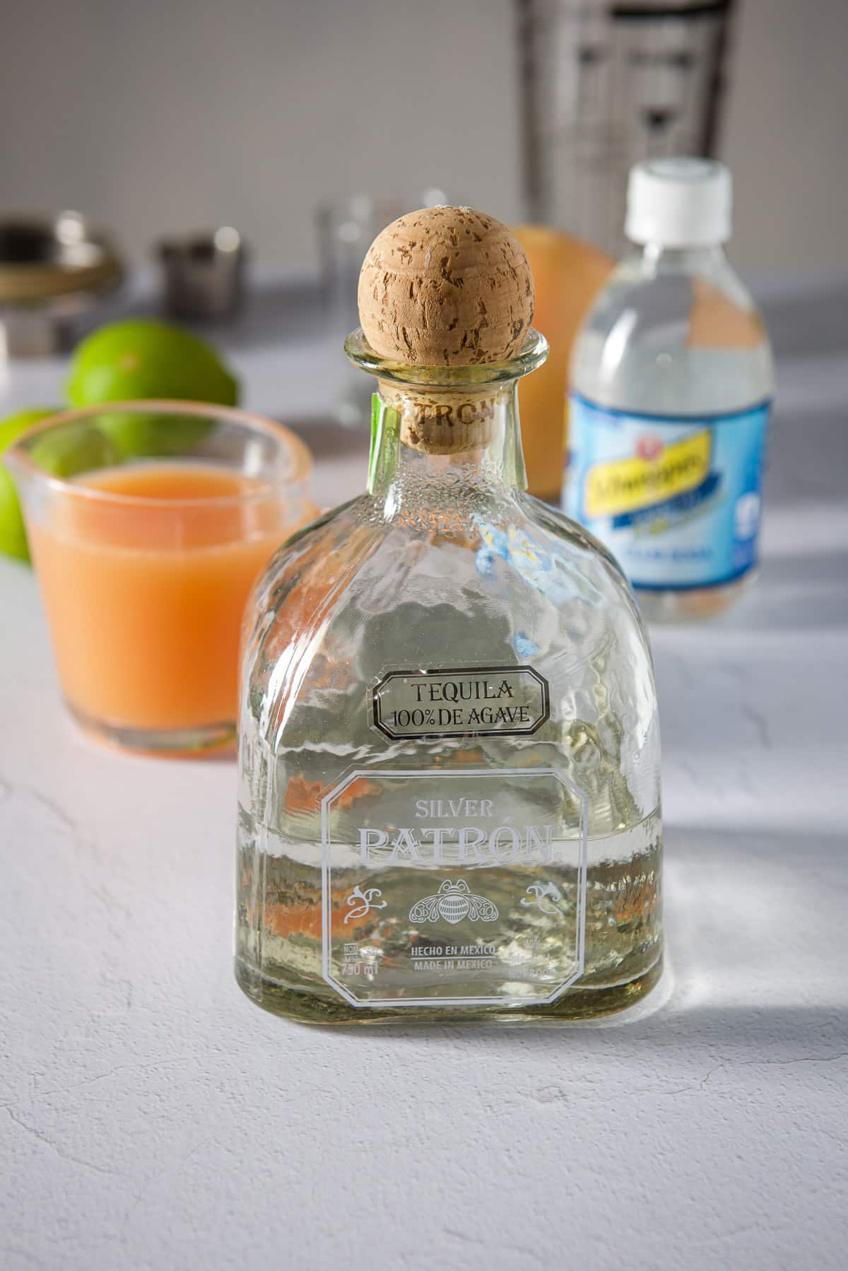 Tequila, grapefruit juice, limes, club soda, a grapefruit and shaker in background
