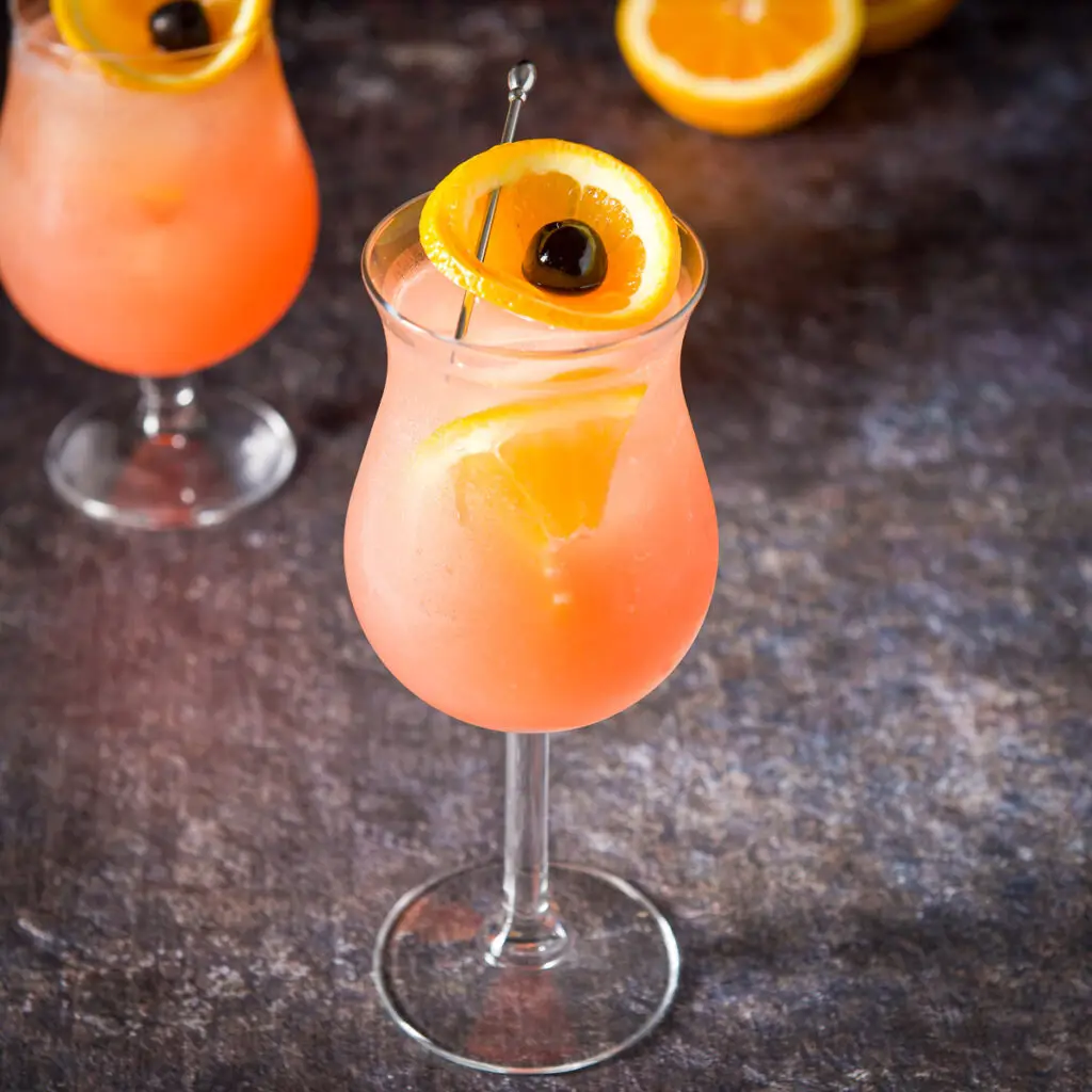 Two tulip glasses filled with the orange cocktail with oranges and cherries as garnish - square