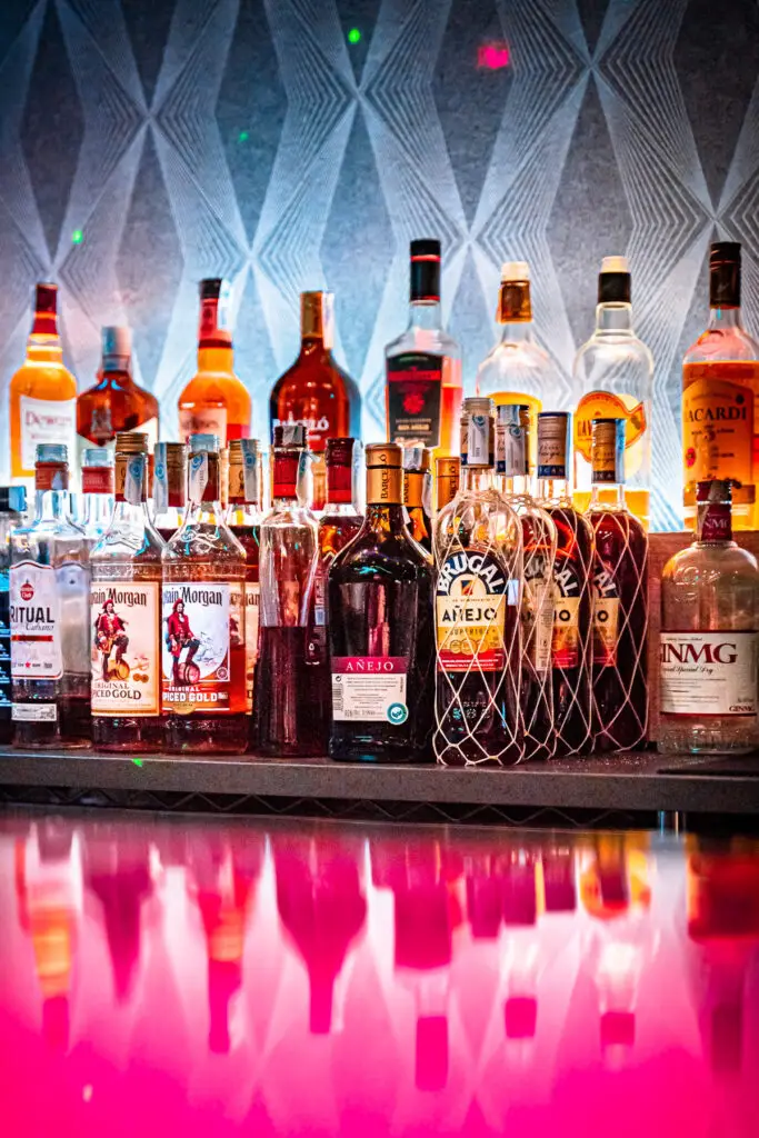 A bunch of alcohol bottles lined up with a vibrant pink table