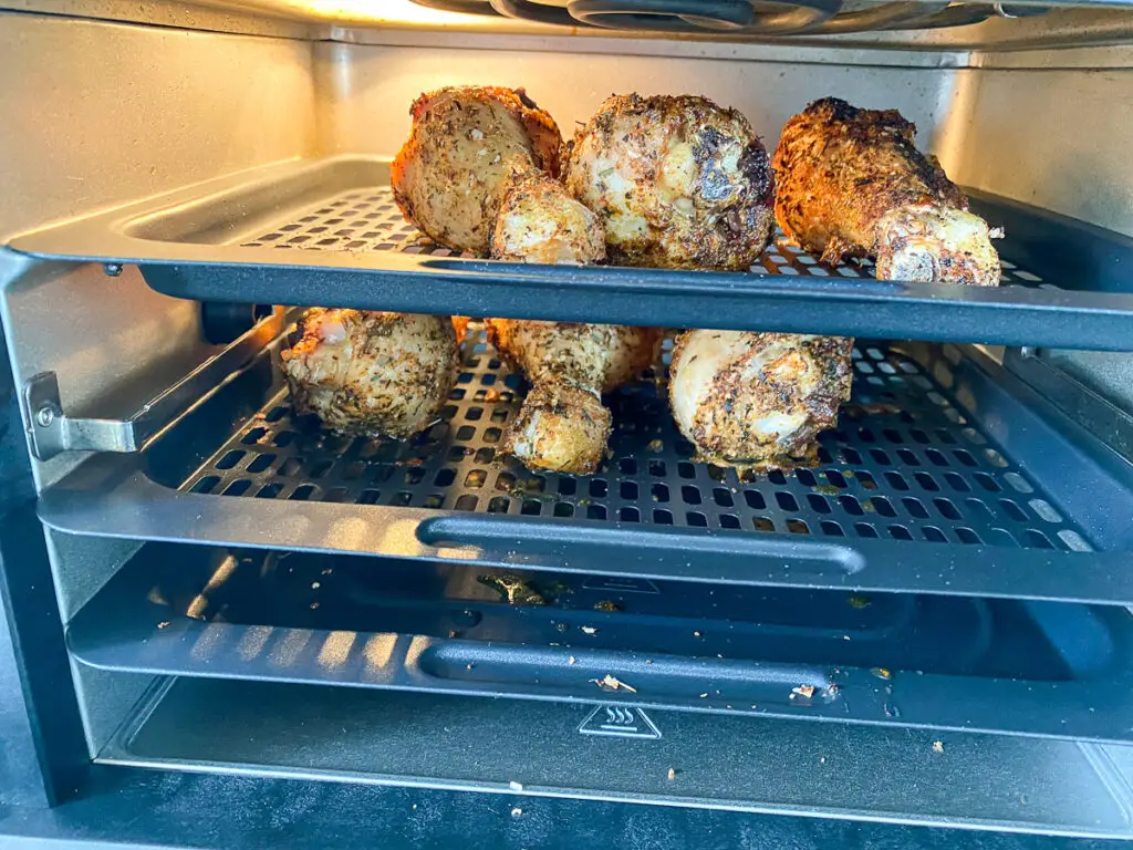 The air fryer open with drumsticks on their trays
