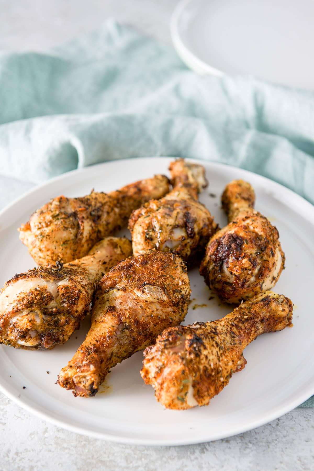 Six drumsticks on a white plate with a napkin and another plate in back