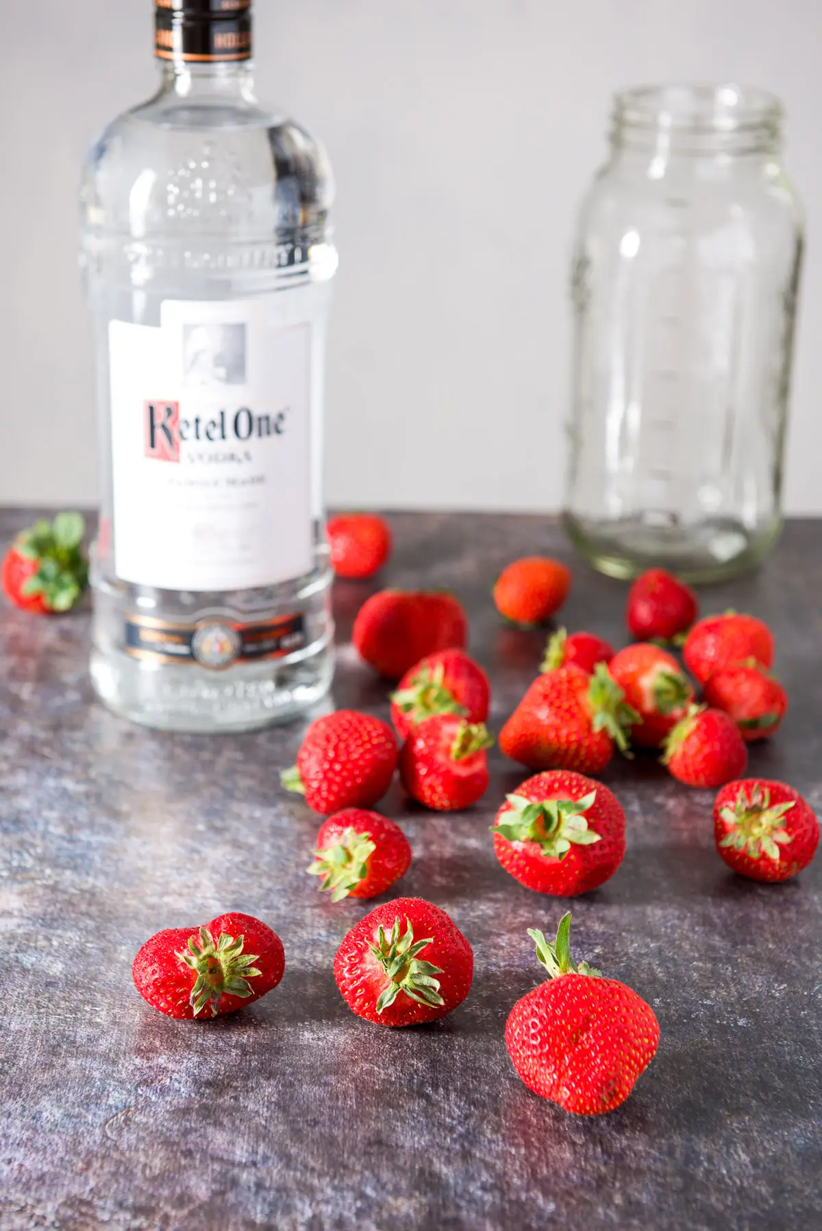 Strawberries on a table with a bottle of vodka along with a large jar