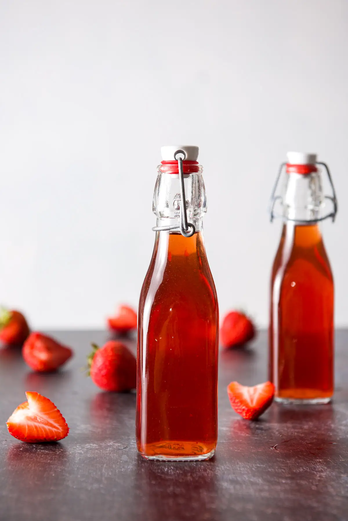 Vertical view of two small bottles of red vodka with strawberries on the table