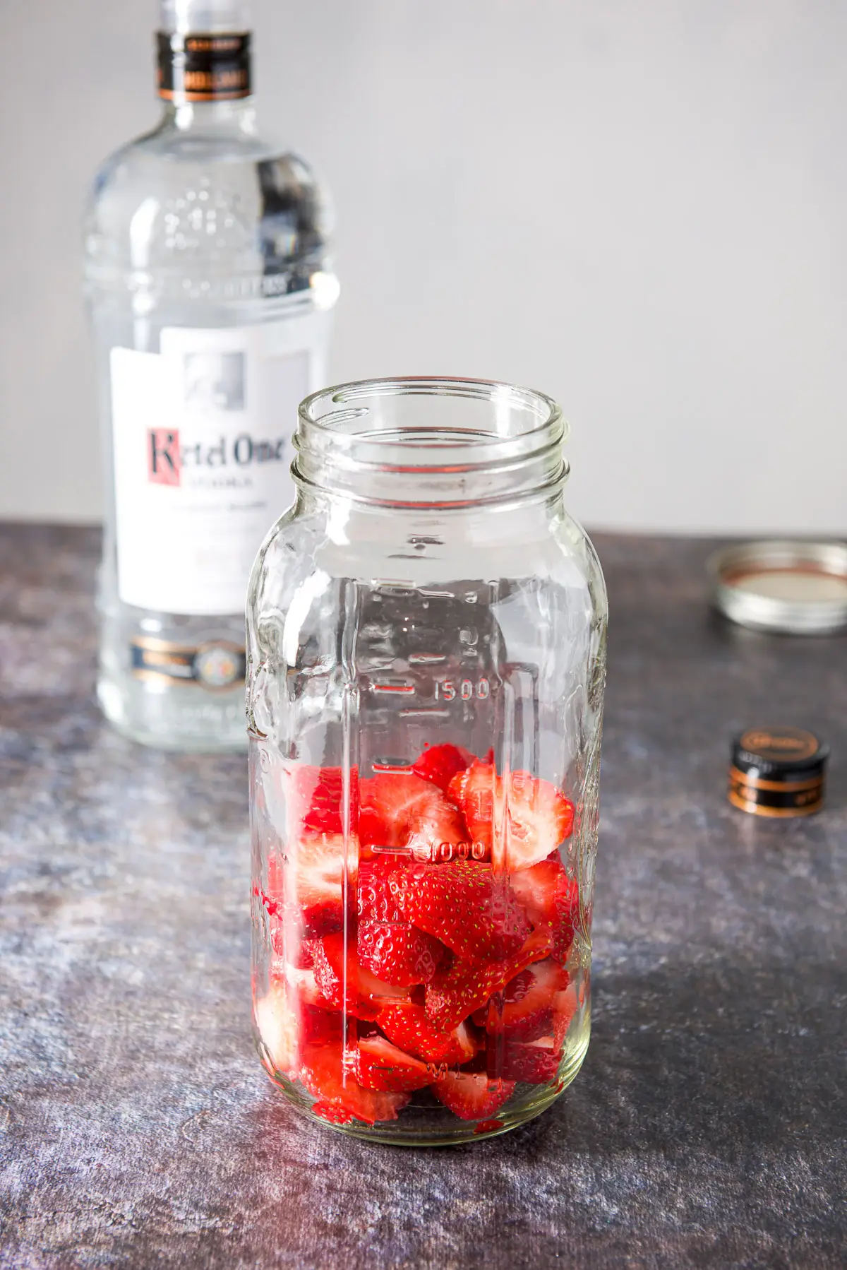 Cut up strawberries in a jar with the bottle of vodka in the background