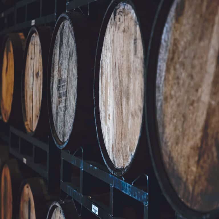 Rows of whiskey filled casks on metal shelves - square