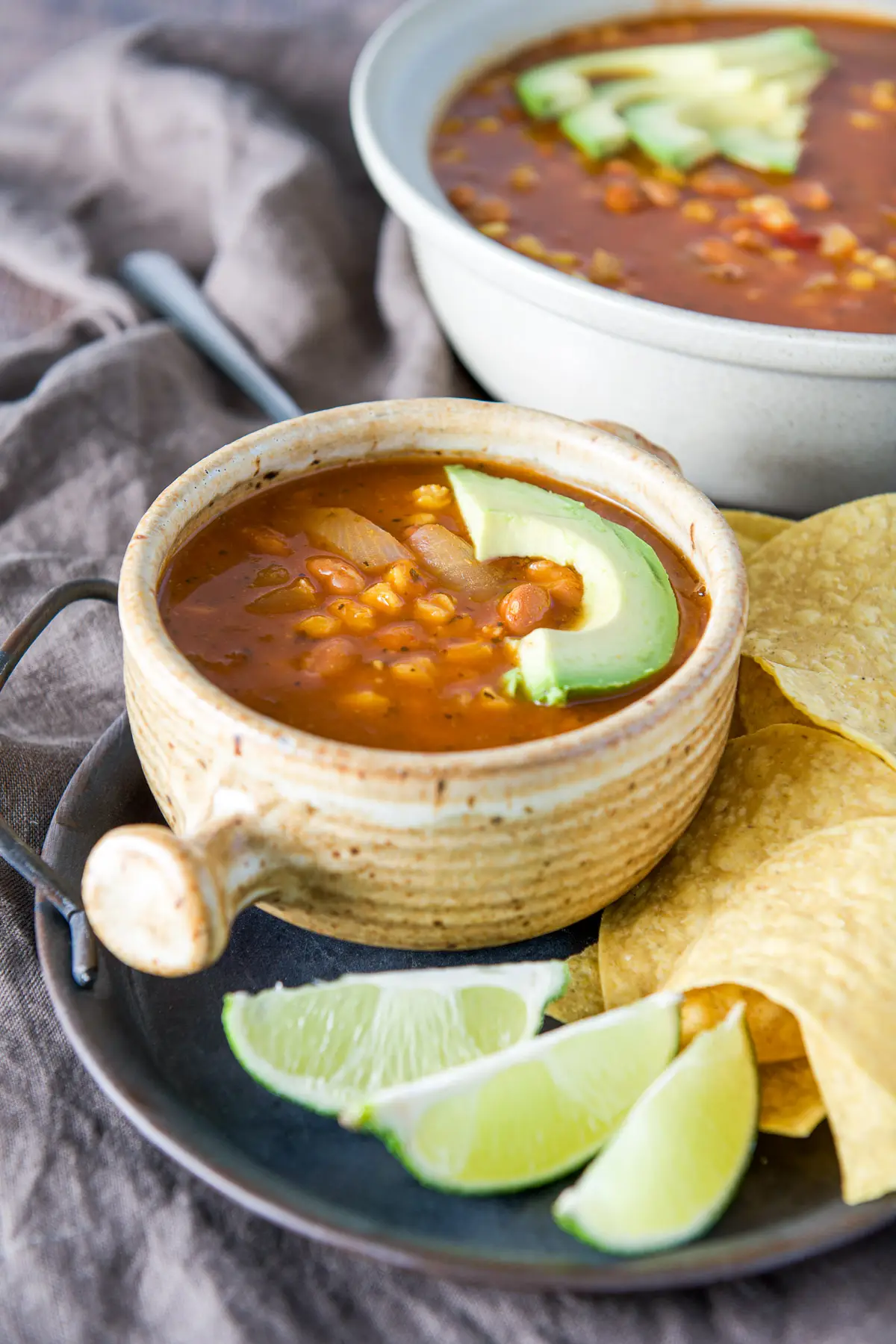 A crock and a big bowl of soup with avocado slices on it as garnish