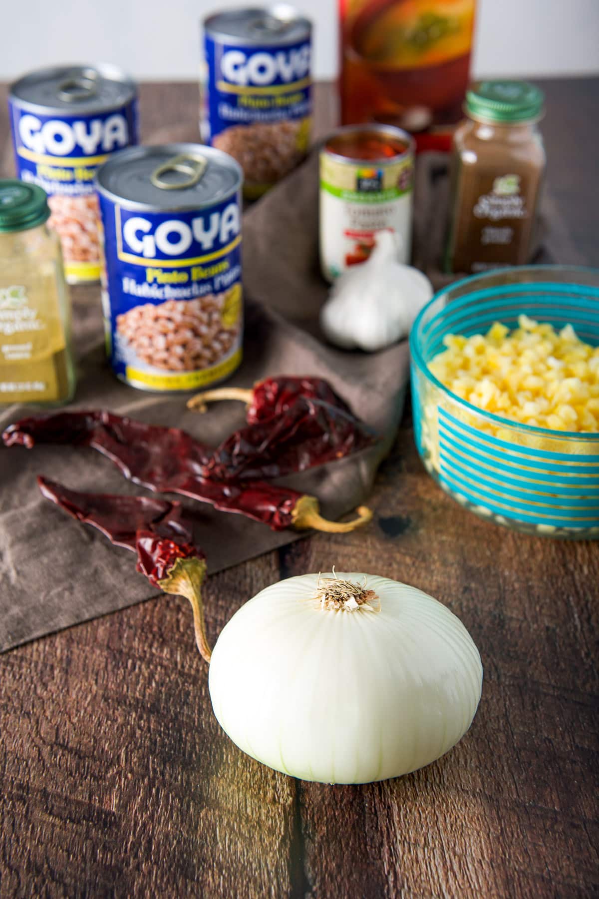 Onion, chiles, bowl of hominy, beans, herbs and spices, broth and tomato paste on a table