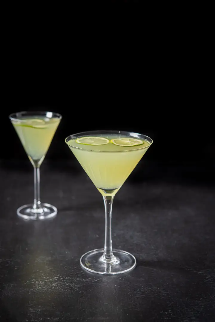Two martini glasses filled with the last word cocktail with lime wheels floating on top